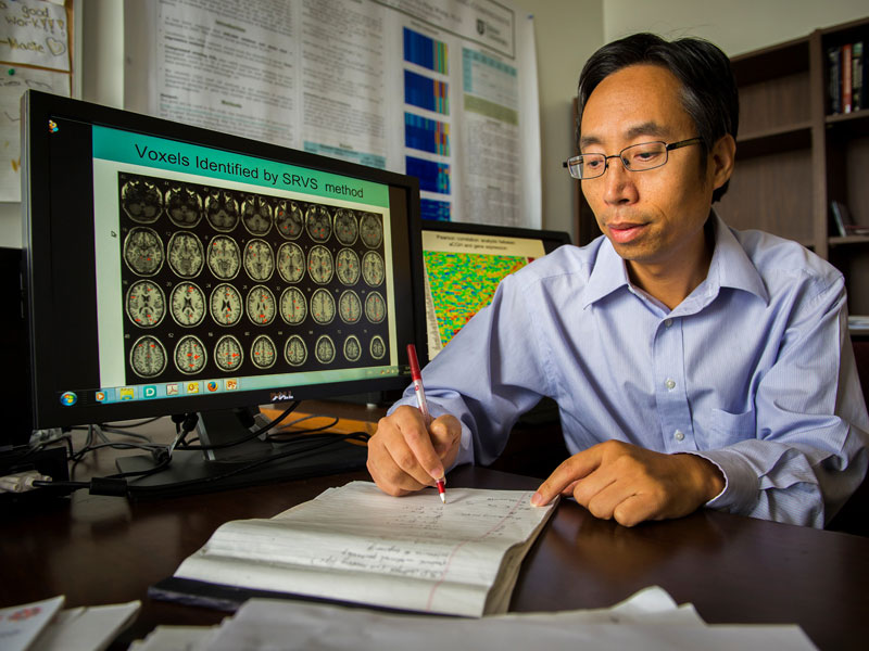Yuping Wang working at a desk, computer monitor shows images of brain scans